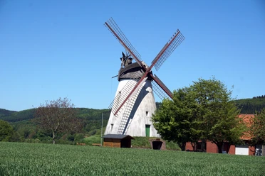Windmühle Struckhof in ländlicher Umgebung mit bewaldeten Hügeln und klarem blauen Himmel im Hintergrund.
