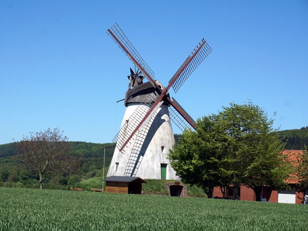 Windmühle Struckhof in ländlicher Umgebung mit bewaldeten Hügeln und klarem blauen Himmel im Hintergrund.