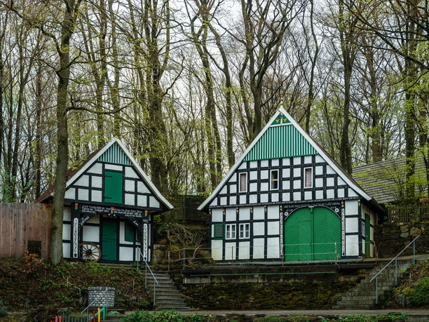 Freilichtbühne Kahle Wart Christoph Partsch (4).jpg Zwei Fachwerkhäuser stehen nebeneinander im Wald, umgeben von kahlen Bäumen, mit grünen Türen.