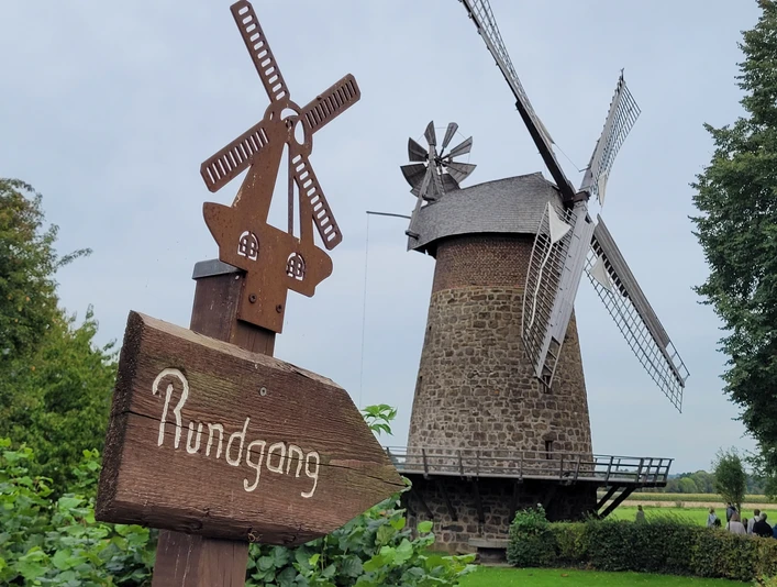 Königsmühle Eilhausen Historische Windmühle aus Stein mit Holzflügeln, umgeben von grüner Landschaft und Hinweisschild.