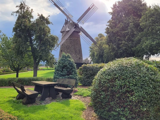 Königsmühle Eilhausen, historische Windmühle in grüner Umgebung, mit Bänken und Tisch im Vordergrund.