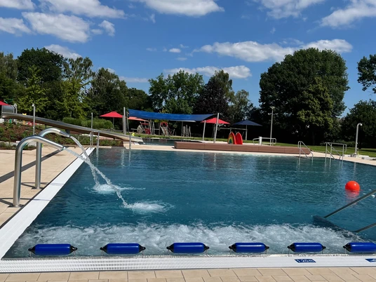 Freibad mit breitem Einstieg, Sprungturm, viel Grün und schattigen Bereichen für entspannte Stunden.