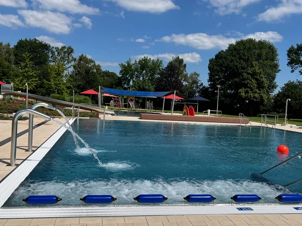 Freibad mit breitem Einstieg, Sprungturm, viel Grün und schattigen Bereichen für entspannte Stunden.