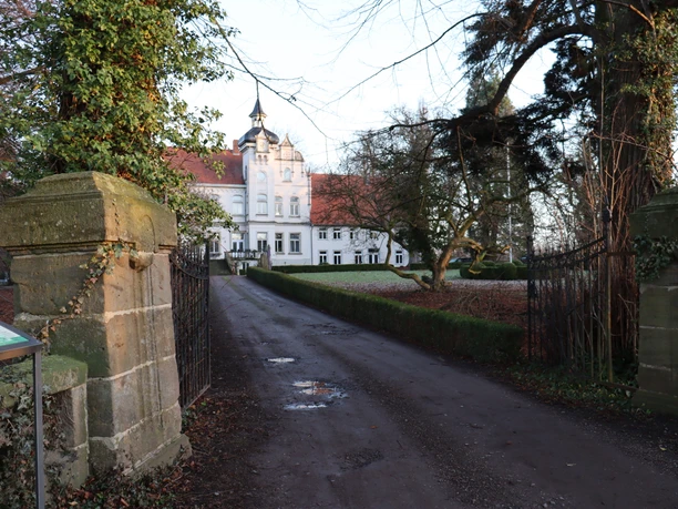 Gut Renkhausen Weißer Herrensitz mit roten Dächern, flankiert von alten Bäumen und einem schmiedeeisernen Tor.