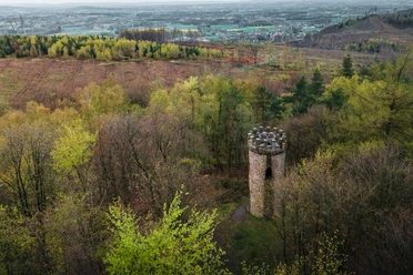 Ein alter, steinernem Turm steht umgeben von einem herbstlich gefärbten Wald im Vordergrund.