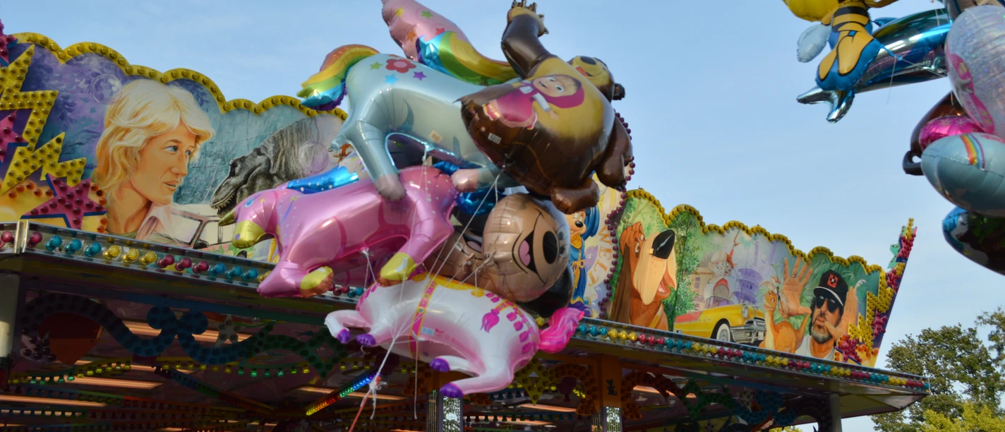 Fehntjer Markt Rhauderfehn Bunte Folienballons in Tierformen vor einem bemalten Fahrgeschäft auf einem Markt.