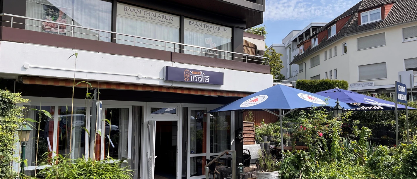 Eingang zum Restaurant Namaste India mit Außenterrasse und Sonnenschirmen