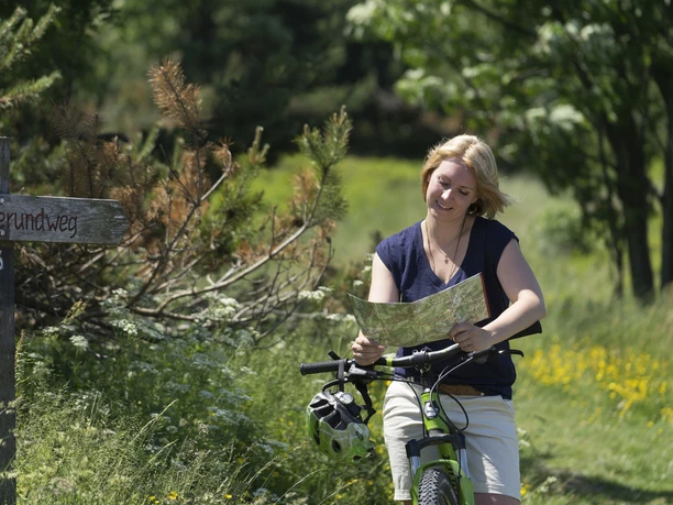 Bikerin mit Fahrradkarte am Wegweiser Bikerin mit Fahrradkarte am Wegweiser