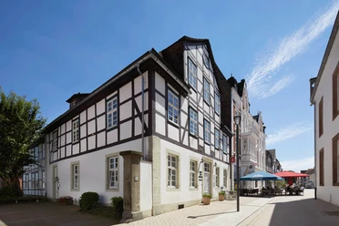 Fachwerkhaus am Marktplatz vor blauem Himmel; nebenan ein Café mit bunten Sonnenschirmen.