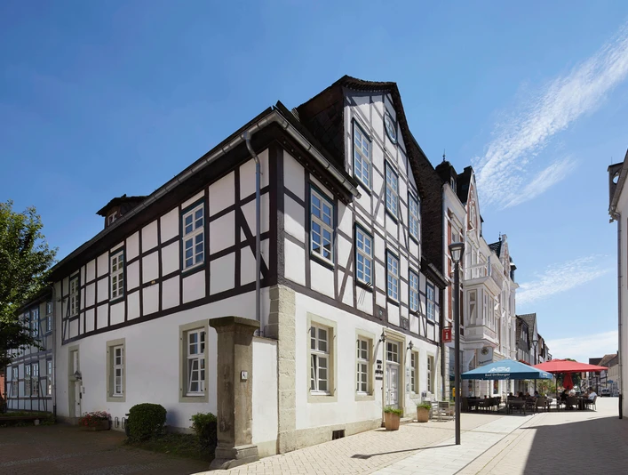Fachwerkhaus am Marktplatz vor blauem Himmel; nebenan ein Café mit bunten Sonnenschirmen.