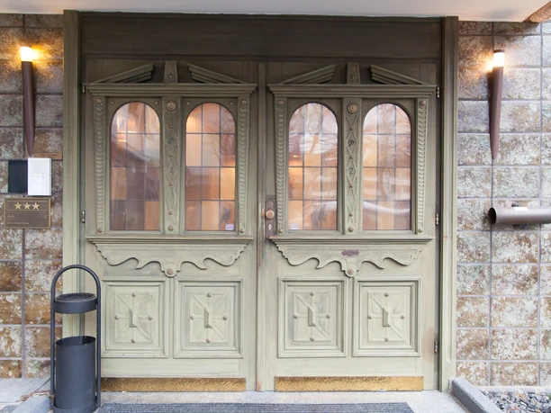 Eingangstür zum Hotel Angerland in Ratingen Massive Holztür mit verzierten Glasfenstern führt in ein elegantes Hotel. Lampen akzentuieren den Eingang.