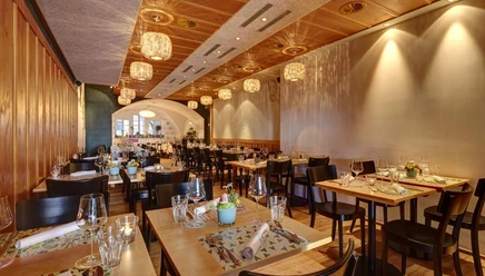 Modern gedeckter Speisesaal im Restaurant Opus mit Holztischen und warmen PendelleuchtenWarmly lit dining room at Restaurant Opus with set tables, wine glasses and wooden ceiling