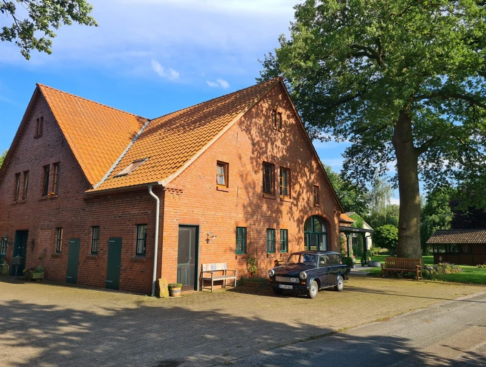 Rotes Backsteinhaus unter strahlend blauem Himmel, mit parkendem schwarzen Auto auf der Einfahrt.