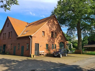 Gottfriedsen_außen.jpg Rotes Backsteinhaus unter strahlend blauem Himmel, mit parkendem schwarzen Auto auf der Einfahrt.