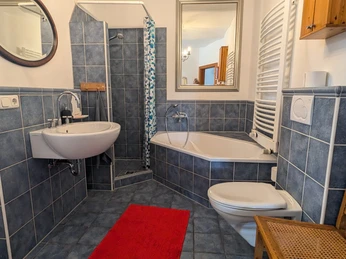 Gottfriedsen_Bad.jpg Badezimmer mit blauen Fliesen, Dusche, Badewanne, Waschbecken und rotem Teppich. Holzmöbel ergänzen.