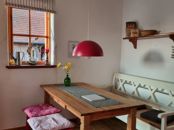 A dining table with wooden bench and red stool, decorated with a yellow vase flower under a red hanging lamp.