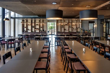 Moderner Speisesaal im Restaurant Vivace mit langen Tischen, Holzdecke und großen Leuchten