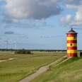 Pilsumer Leuchtturm Roter und gelber Leuchtturm auf grünem Deich mit weitem Himmel und Windrädern im Hintergrund.