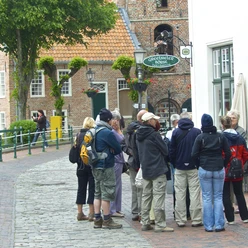 En gruppe mennesker på en guidet tur i Greetsiel foran restauranten Greetsieler Börse med kirken i baggrunden.
