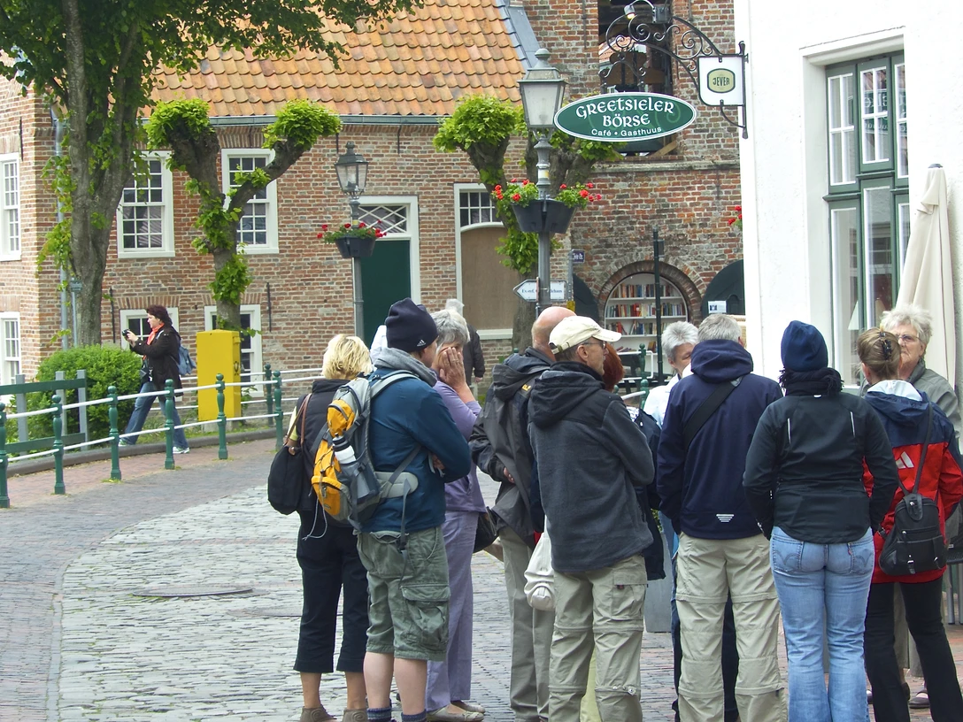 Dorfführung Greetsiel Eine Gruppen Menschen bei einer Dorfführung durch Greetsiel, vor dem Restaurant Greetsieler Börse, im Hintergrund die Kirche.
