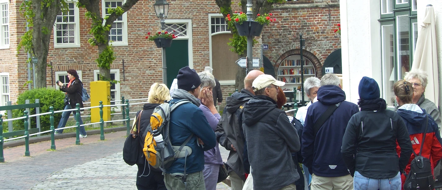 Een groep mensen tijdens een rondleiding door Greetsiel, voor het restaurant Greetsieler Börse, met de kerk op de achtergrond.