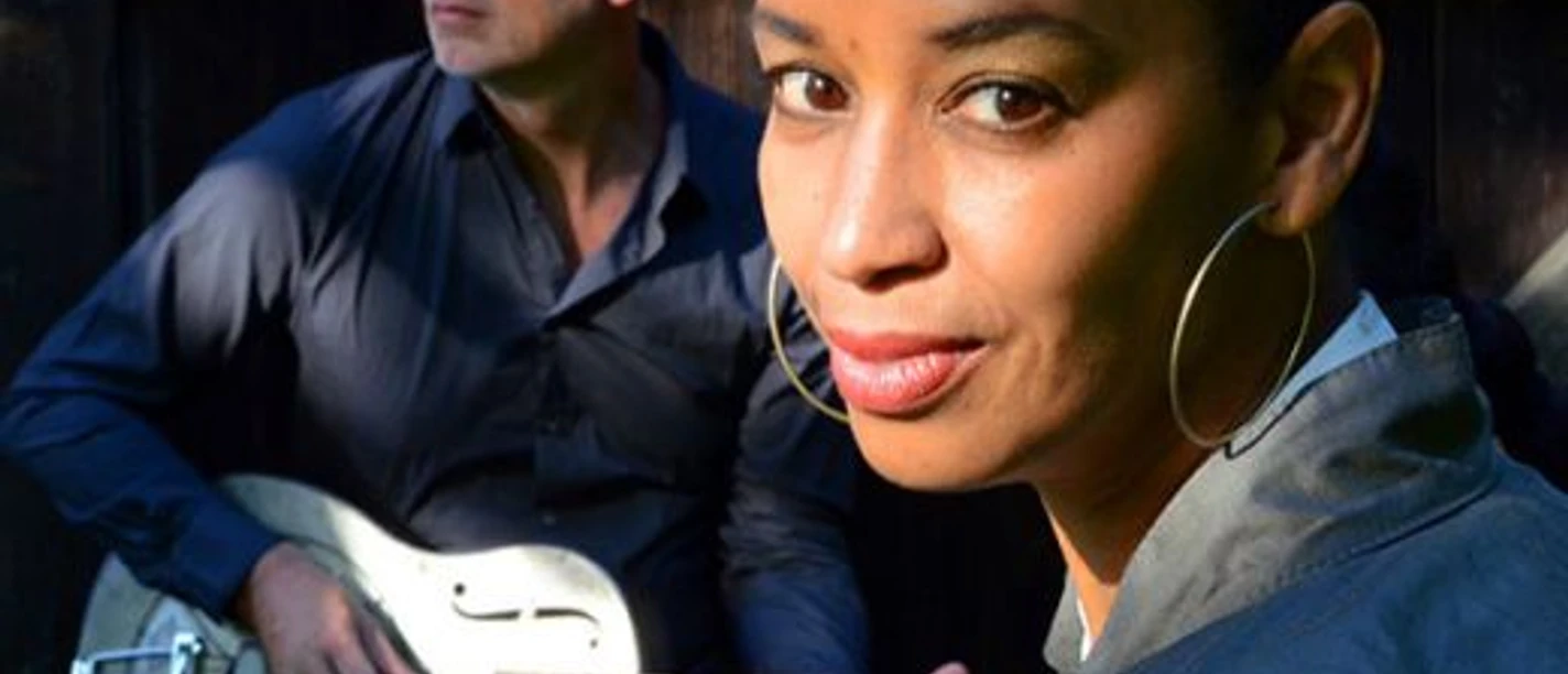 Friend N Fellow Zwei Musiker, eine Frau mit großen Ohrringen im Vordergrund und ein Mann mit Gitarre im Hintergrund