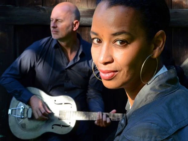 Friend N Fellow Zwei Musiker, eine Frau mit großen Ohrringen im Vordergrund und ein Mann mit Gitarre im Hintergrund