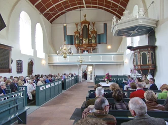 Kirche in Uttum Innenraum der Kirche in Uttum. Menschen sitzen in den Kirchenbänken. Blick auf die schöne Orgel.