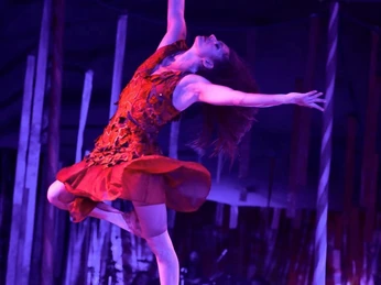 Aachener Weihnachtscircus 2024_Tatiana Ozhiganova2.jpg Eine Zirkusartistin in einem leuchtend roten Kleid schwebt am Seil durch die Luft in blau-violettem Licht.