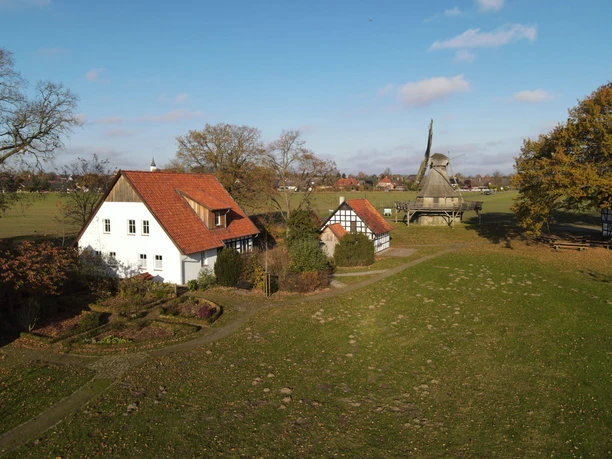 Rural scene with a traditional mill and historic half-timbered houses surrounded by greenery.