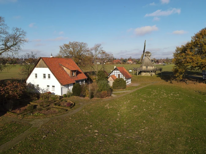 Landelijk tafereel met een traditionele molen en historische vakwerkhuizen omgeven door groen.