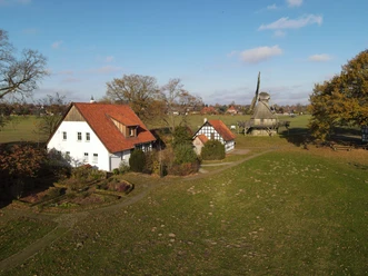 Mühlengelände 2021-11 (2).jpeg Ländliche Szene mit einer traditionellen Mühle und historischen Fachwerkhäusern im Grünen.
