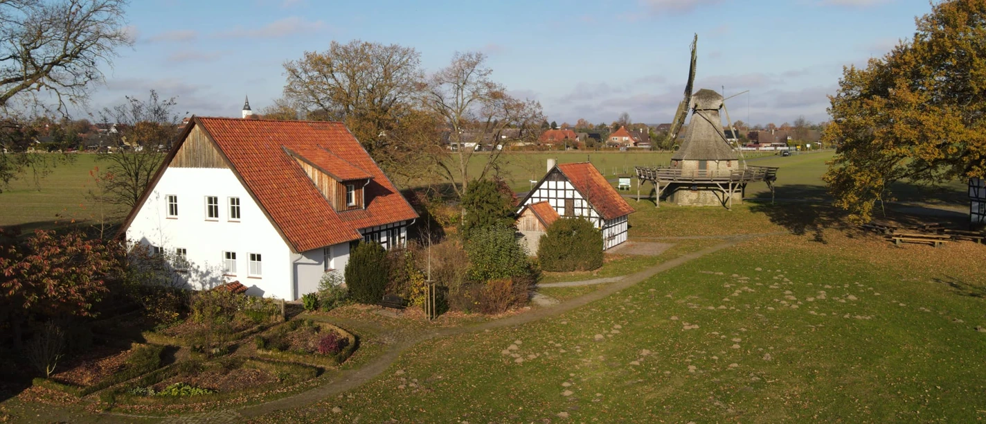 Mühlengelände 2021-11 (2).jpeg Ländliche Szene mit einer traditionellen Mühle und historischen Fachwerkhäusern im Grünen.