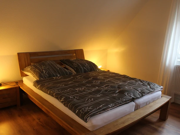 IMG_1191.JPG Schlafzimmer mit einem großen Doppelbett aus Holz, Parkettboden und sanfter Beleuchtung.