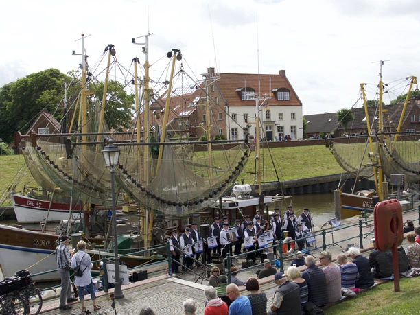 Sonntagskonzert im Hafen Greetsiel Ein Shanty-Chor singt vor historischen Krabbenkuttern im Hafen von Greetsiel für zahlreiches Publikum.