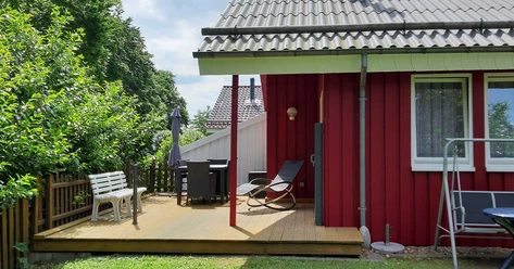 Ferienpark Extertal_Das Waldhaus Ein rotes Holzhaus mit Terrasse, Gartenmöbeln und Liegestühlen, umgeben von grüner Natur.