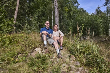 LeistruperWald-LeistruperWaldRoute-LeistruperWald-LTMGmbH-HirschmeierMediaGmbH&CoKG_059.jpg Zwei Personen sitzen auf einer Steinbank im Wald und genießen die sonnige Atmosphäre umgeben von Bäumen.