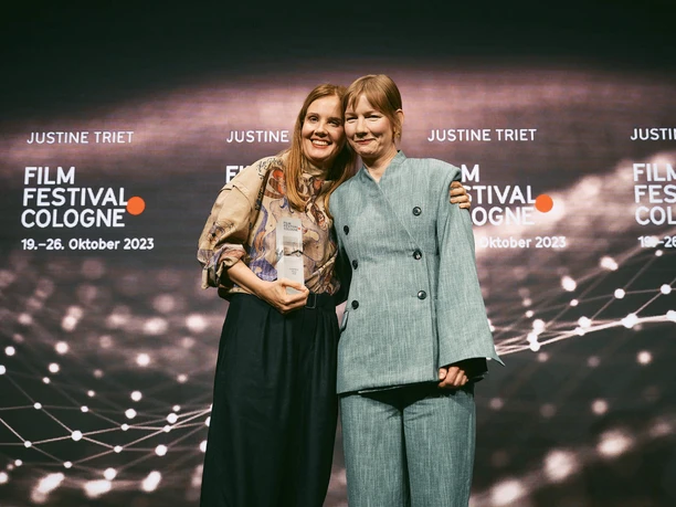 Film Festival Cologne Auf der Bühne des Film Festival Cologne halten zwei Frauen in festlicher Kleidung einen Award. Lächelnd.