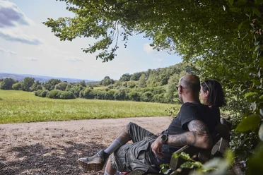 Dörentrup-NABULehrpfad-Teutoburger Wald-LTMGmbH-HirschmeierMediaGmbH&CoKG_025.jpg Ein Paar sitzt auf einer Bank am Waldrand und blickt über eine weitläufige Wiesenlandschaft.