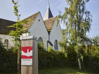 Kalletal-TallerBergrunde-TeutoburgerWald-LTMGmbH-HirschmeierMediaGmbH&CoKG_137.jpg Eine Kirche umgeben von Bäumen, im Vordergrund ein Wegweiser der Taller Bergrunde.