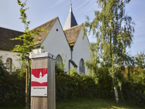 Kalletal-TallerBergrunde-TeutoburgerWald-LTMGmbH-HirschmeierMediaGmbH&CoKG_137.jpg Eine Kirche umgeben von Bäumen, im Vordergrund ein Wegweiser der Taller Bergrunde.
