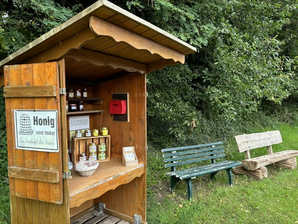 Die Honighütte ©Emsland Tourismus GmbH Kleine Holzhütte mit Honiggläsern und Geldkassette neben zwei Bänken am Waldrand.