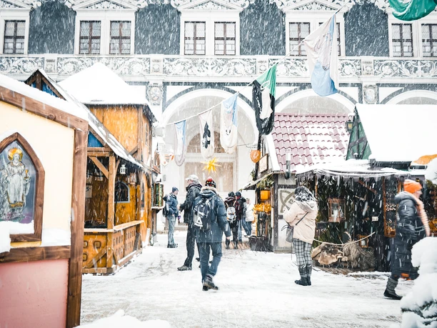 Weihnachtsmarkt im Stallhof Dresden (2).jpg Winterlicher Weihnachtsmarkt im Stallhof Dresden, mit Verkaufsständen und schneebedeckten Menschen.