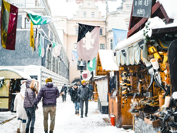 Weihnachtsmarkt im Stallhof Dresden (1).jpg Verschneiter Weihnachtsmarkt in Dresden mit Besuchern, Ständen und historischen Gebäuden im Hintergrund.