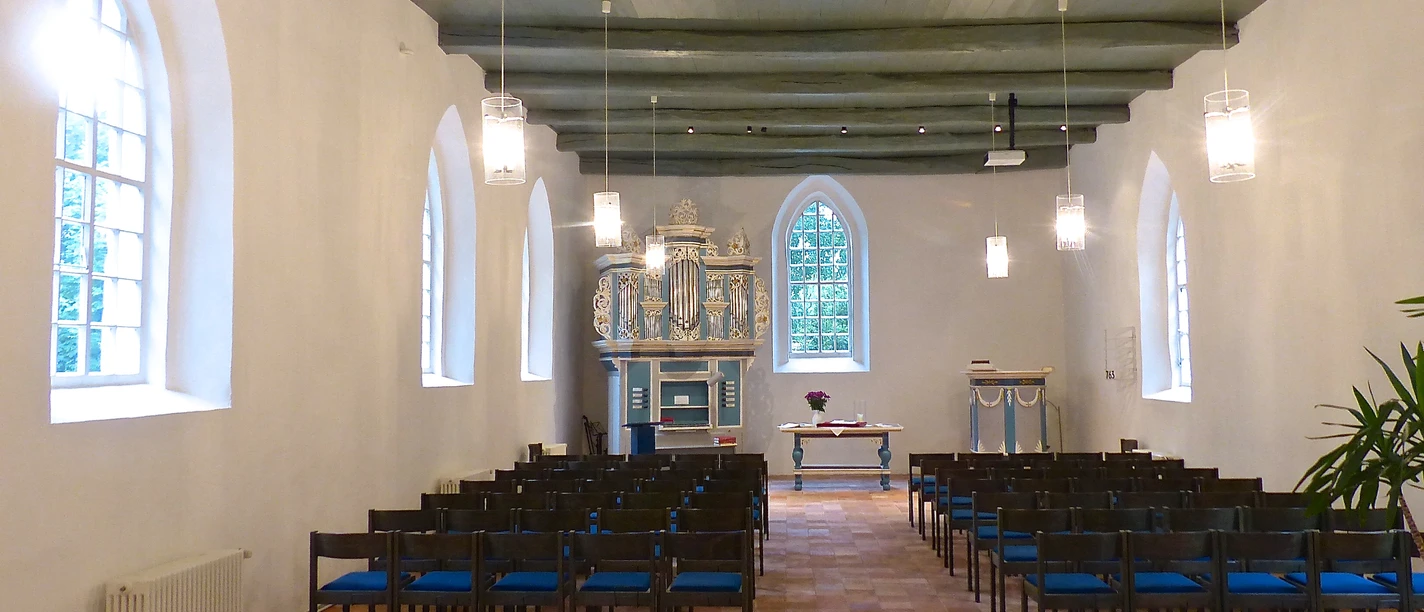 Kirche in Jennelt Heller Kirchenraum mit Holzbalkendecke, Stuhlreihen und einer blau-goldenen Orgel im Altarbereich.