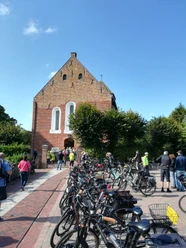 Krummhörner Kirchturm Tour 2018 Radfahrerinnen und Radfahrer versammeln sich vor der Backsteinkirche Jennelt bei sonnigem Wetter.