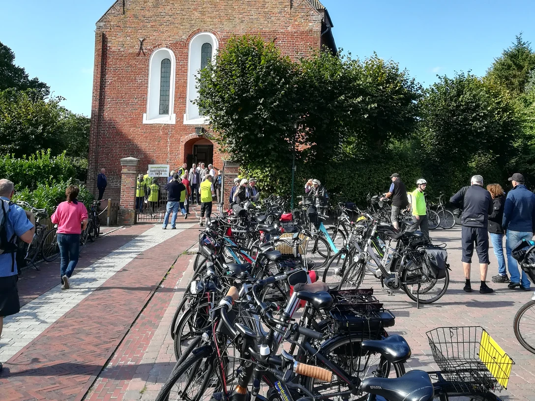 Krummhörner Kirchturm Tour 2018 Radfahrerinnen und Radfahrer versammeln sich vor der Backsteinkirche Jennelt bei sonnigem Wetter.