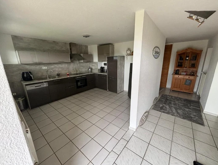 Küche_Flur.jpg Moderne Küche mit grauen Einbauschränken, Herd und Kühlschrank, angrenzend an Flur mit Sideboard.