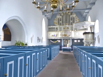 Kirche Manslagt Heller Kircheninnenraum mit blauen Holzbänken, weißer Kanzel und prunkvoller Orgel.