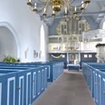 Kirche Manslagt Heller Kircheninnenraum mit blauen Holzbänken, weißer Kanzel und prunkvoller Orgel.